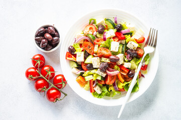 Greek salad. Vegetable salad with tomato, cucumber, feta cheese and olive oil. Top view on white stone table.