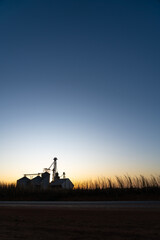 Naklejka premium Beautiful silhouette view of silos in soybean farm and corn plantation at sunset on BR-163 road. Mato Grosso, Brazil. Concept of agriculture, ecology, environment, logistics, industry.