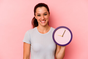 Young caucasian woman holding a clock isolated on pink background happy, smiling and cheerful.