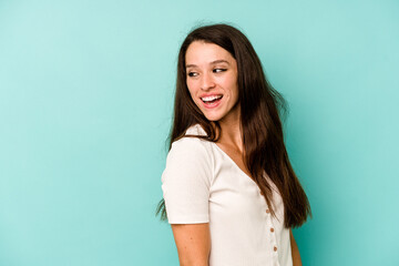 Young caucasian woman isolated on blue background looks aside smiling, cheerful and pleasant.