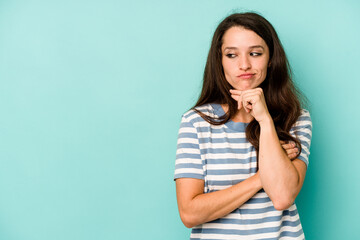 Young caucasian woman isolated on blue background looking sideways with doubtful and skeptical expression.