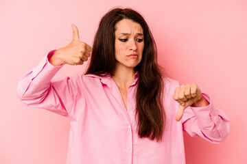 Young caucasian woman isolated on pink background showing thumbs up and thumbs down, difficult choose concept