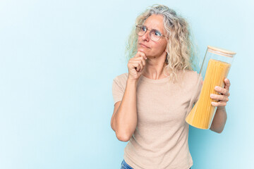 Middle age caucasian woman holding a spaghettis jar isolated on blue background looking sideways with doubtful and skeptical expression.