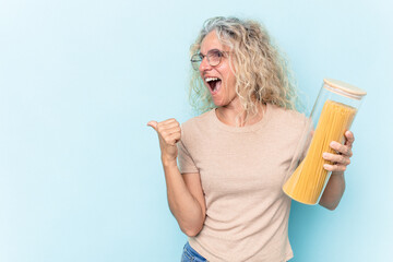 Middle age caucasian woman holding a spaghettis jar isolated on blue background points with thumb finger away, laughing and carefree.