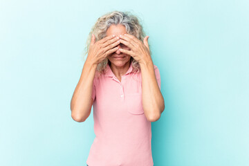 Middle age caucasian woman isolated on blue background afraid covering eyes with hands.