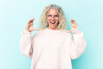 Middle age caucasian woman isolated on blue background holding something with palms, offering to camera.