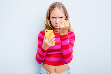 Caucasian teen girl holding mobile phone isolated on blue background showing fist to camera,...