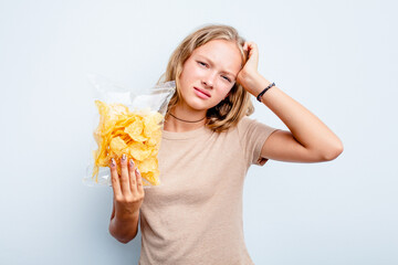 Caucasian teen girl holding bag of chips isolated on blue background being shocked, she has remembered important meeting.