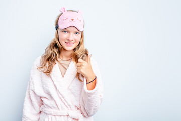 Caucasian teen girl wearing a pajama isolated on blue background smiling and raising thumb up