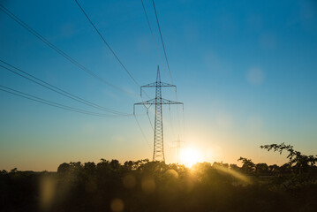 Fototapeta premium high-voltage line over at sunset, tree alley silouette