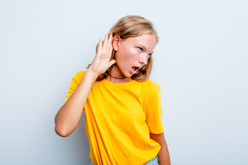 Caucasian teen girl isolated on blue background trying to listening a gossip.