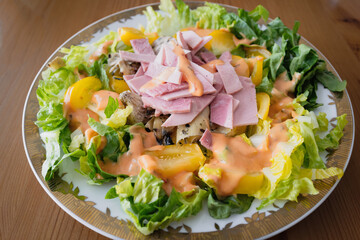 Ham, artichokes and orange tomatoes making a salad meal with lettuce and salad sauce.