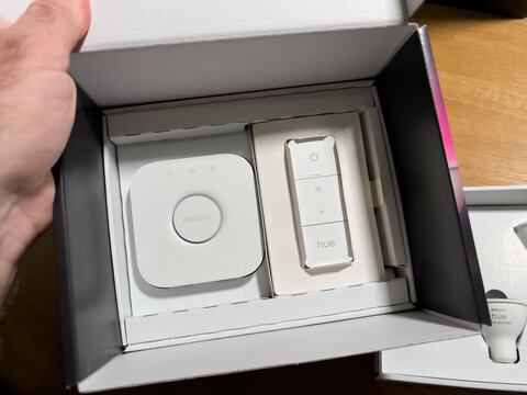 Paris, France - Dec 14, 2021: POV male hand unboxing set of new Philips Hue Bridge with remote control switch and three GU10 bulbs with white and color capabilities