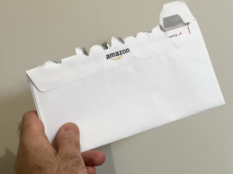 London, United Kingdom - Jan 3, 2022: Rear view of Amazon open postal envelope in male hand - marketing communication from the company founded by Jeff Bezos