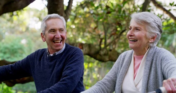Happy, active and retired senior couple enjoying a walk with their bicycles through a park while laughing and having fun. Happy elderly man and woman talking and enjoying a active date outdoors