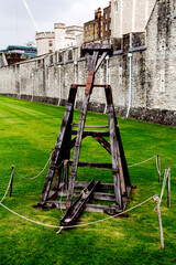 on a green lawn near the walls of the Tower of London, an old catapult is presented