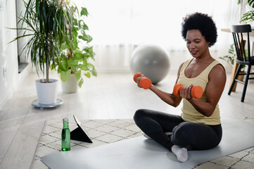 Fototapeta na wymiar African-American woman doing exercises on the floor at her home. Trying to stay healthy and fit.