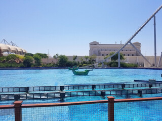 a swimming pool with clear blue water and two boats in the center, as elements of an attraction in an amusement park