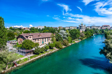 Fototapeta na wymiar BERN, SWITZERLAND - August 2nd 2022: The Federal Palace of Switzerland (Bundeshaus) and people enjoying river life to beat the summer heat.