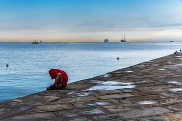 red dressed boy sitting on the edge of a pier in trieste, italy