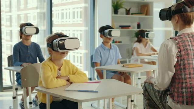 Experience augmented reality in a school. Teacher with pupils wearing VR glasses to watch videos and study together. People and technology concept.