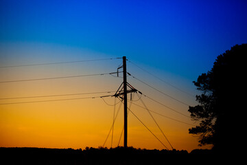 A tower with power lines from a nuclear power plant in Ukraine against the background of a sunset with the colors of the flag of Ukraine.