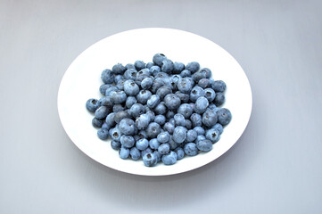 bunch of blueberry berries in a white plate on a gray background