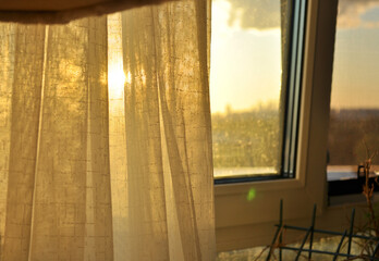Sultry summer outside the window with the setting sun through curtains with an abstract background