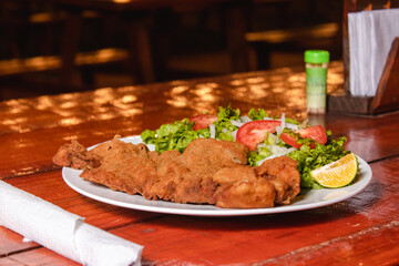 A plate of milanesa with salad on a wooden table.