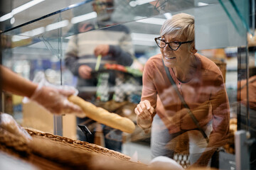 Happy senior woman choosing pastry at supermarket bakery.