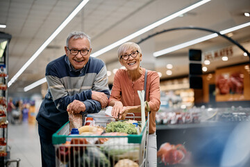 Happy senior couple enjoys in shopping at supermarket and looking at camera.