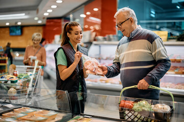 Happy supermarket manager assists senior man in choosing meat packages.