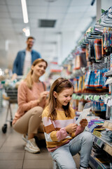 Happy little girl shopping school supplies with her parents in store.