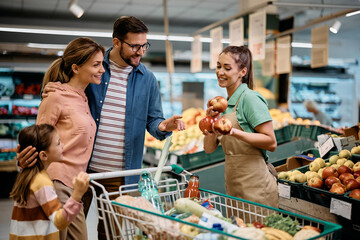 Happy family talks to saleswoman while buying fruit in supermarket.