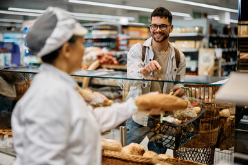 Young happy man buying bread in supermarket bakery.