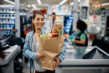 Happy woman with paper bag full of groceries in supermarket.