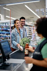 Young happy couple talks to cashier at supermarket checkout.