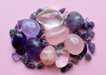 Gemstone minerals on a pink background. Round tumbling amethyst minerals, amethyst crystal and rose quartz.