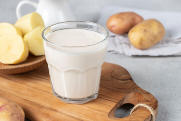 Vegan potato milk in glass and potato in plate on wooden board. Plant based milk replacer and lactose free