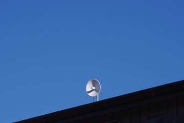 Fototapeta na wymiar A single white dish antenna on a rooftop under bright blue sky