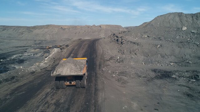 Top view of yellow dump truck with garbage rock in coal mining. Road to processing plant from copter