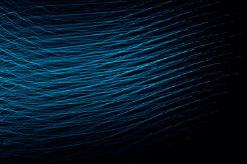 Photo of light rays, stripes of wave lines with blue light, speed and motion blur. Abstract digital flare, iridescent glare over black background.
