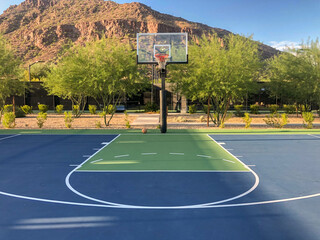 Mountain side blue and green outdoor basketball court with ball.