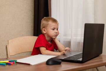 Online distance learning. The child looks carefully at the laptop and studies the drawing lesson online on the Internet. Online school.