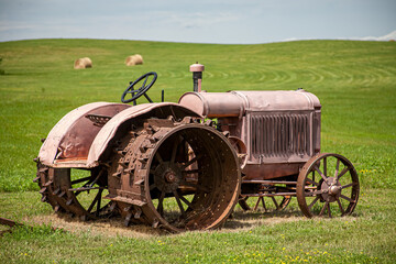 a vintage tractor sits out in a field of a farm with hay bails