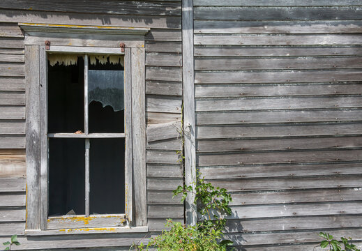 a broken window on the wall of on hold schoolhouse with weathered siding