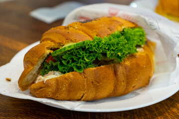 Croissant sandwich with cream cheese, meat and vegetables on a white plate. Concept of healthy breakfast