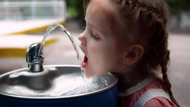 toddler baby girl quenches the thirst with drinking water fountain at the park