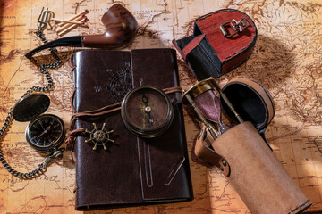 flat lay leather journal compass pocket watch sand timer and pipe on old world map