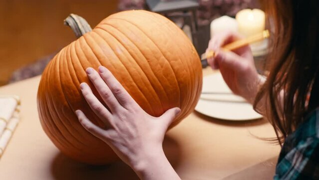 Preparing pumpkin for Halloween. Woman sitting and marking pumpkin with pencil before carving halloween Jack O Lantern at home for her family.